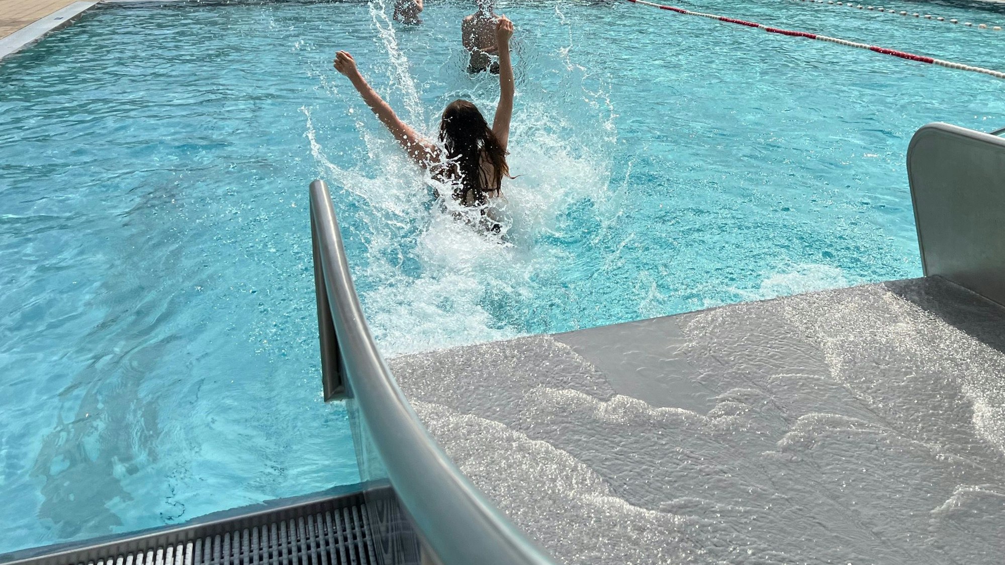 Eine junge Frau rutscht mit den Armen nach oben von der Rutsche ins Becken.
