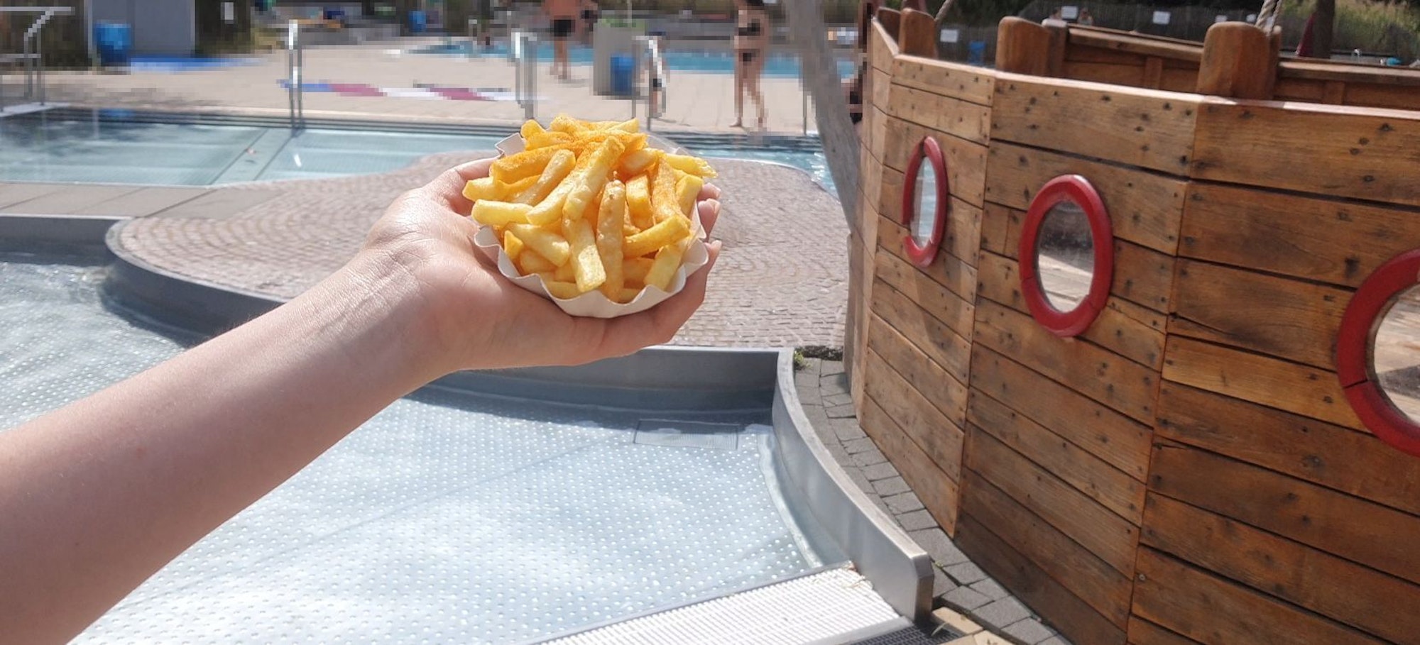 Eine Schale Pommes wird vor das Kinderbecken im Höhenbergbad in die Kamera gehalten.