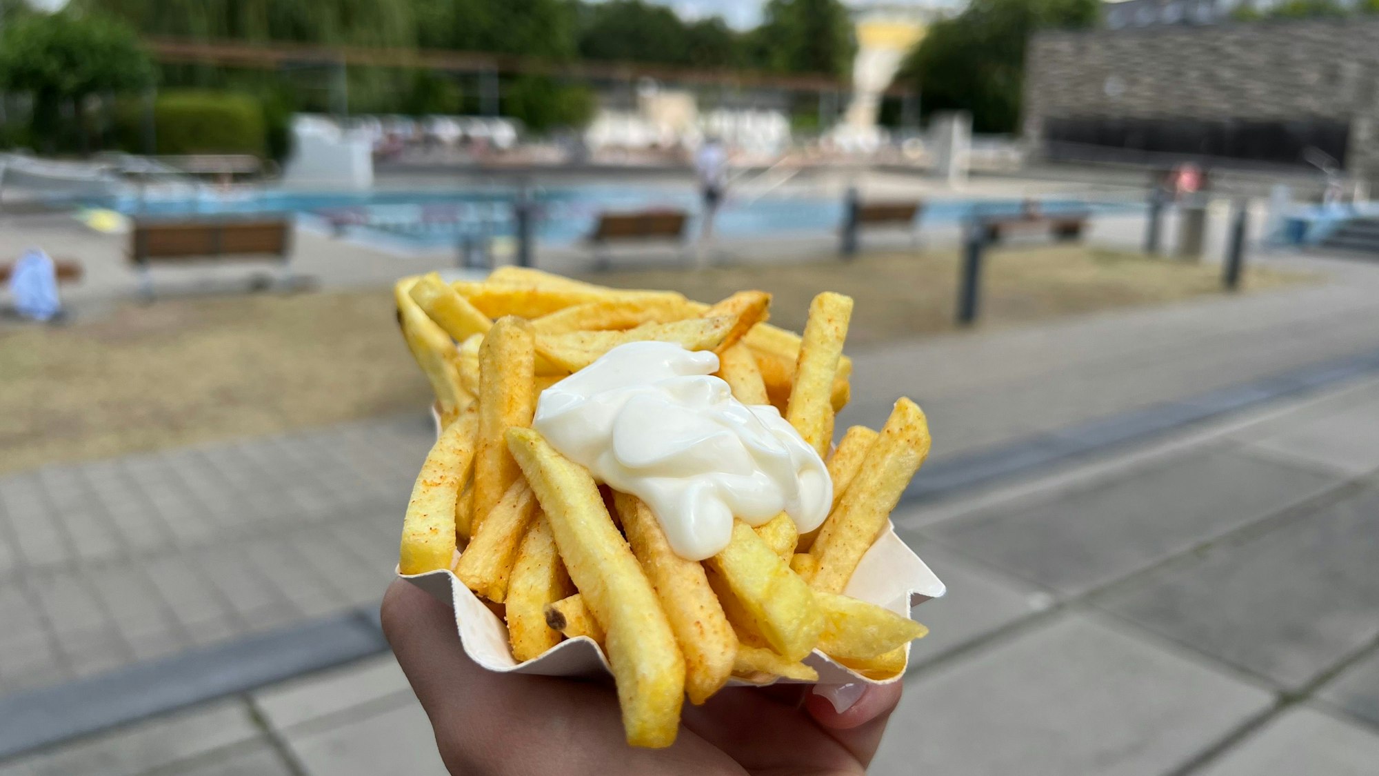 Eine Schale Pommes mit Mayo wird vor das Schwimmbecken gehalten.