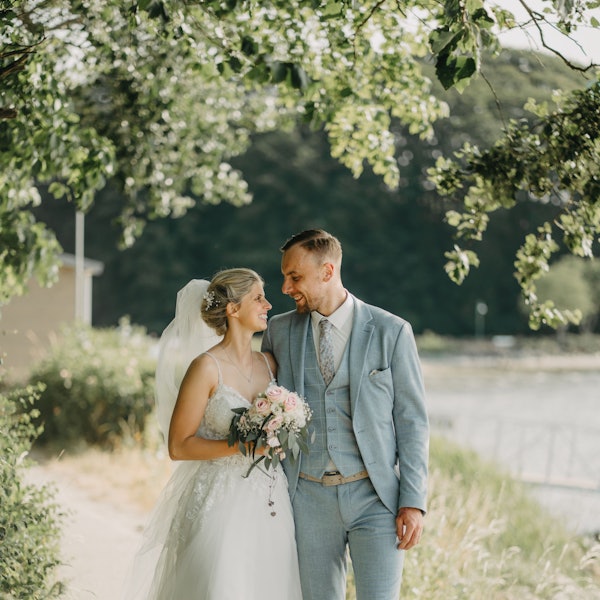 Ein Brautpaar steht im Grünen und lächelt sich an.