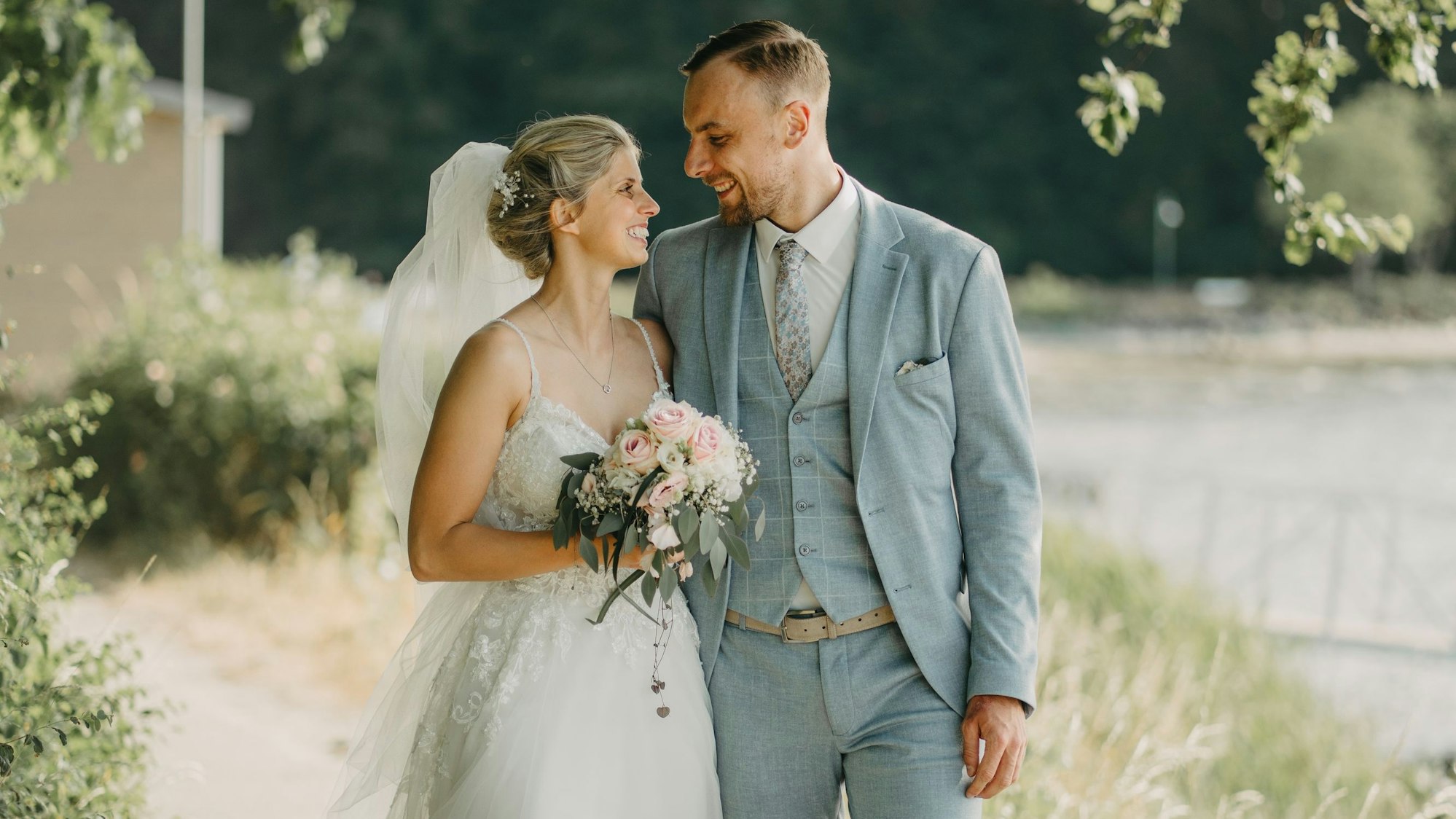 Ein Brautpaar steht im Grünen und lächelt sich an.