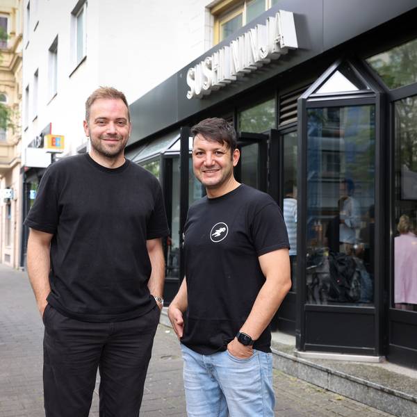 David Keuenhof und Sofien Kouraichi stehen vor einem von drei Kölner Sushi-Ninja-Restaurants. Sie tragen dunkle T-Shirts.