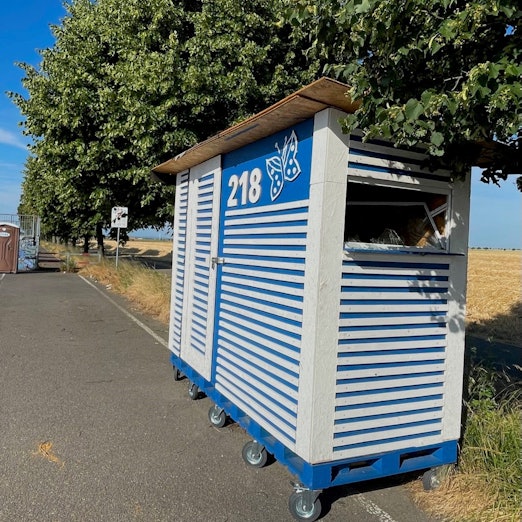 An einer Straße steht ein blau-weiß gestreiftes Häuschen.