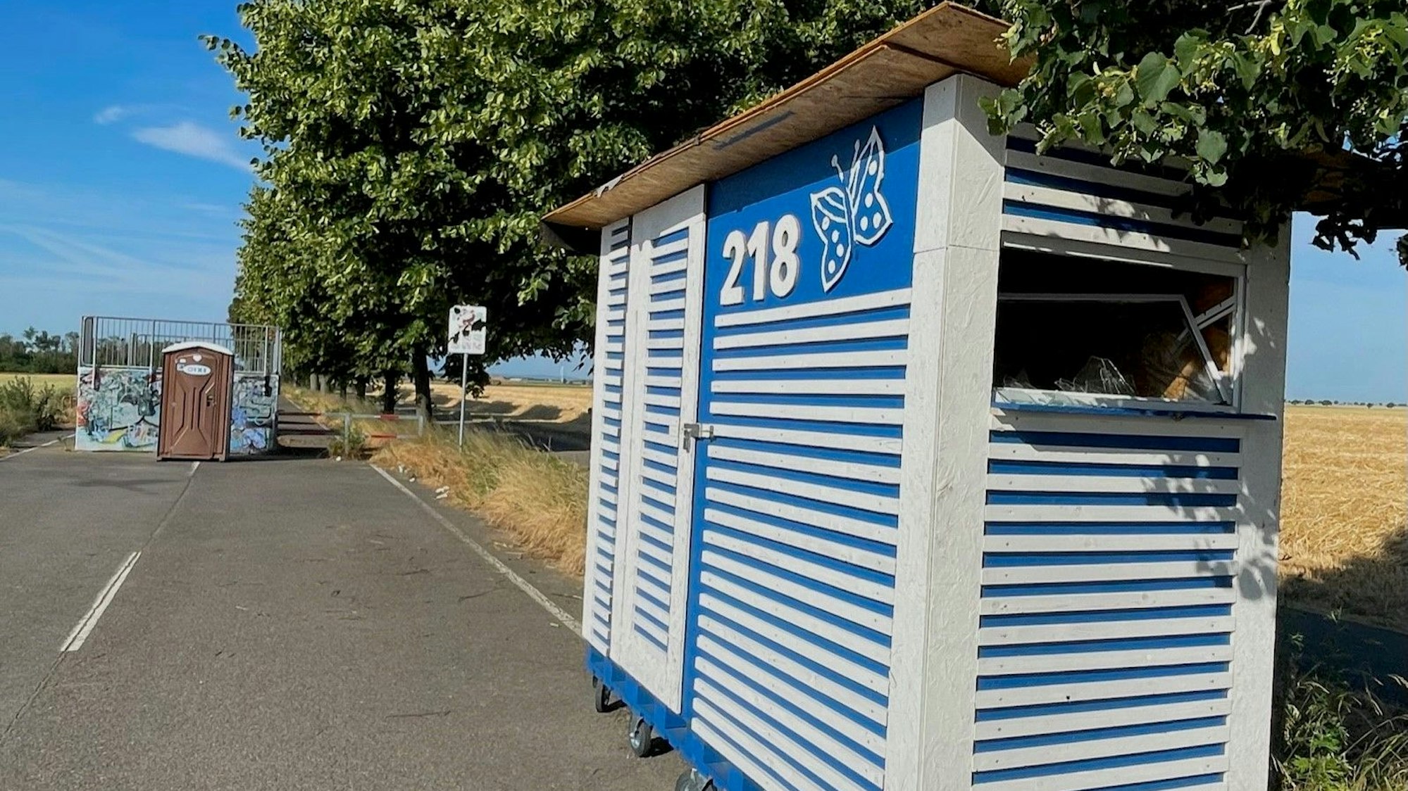 An einer Straße steht ein blau-weiß gestreiftes Häuschen.