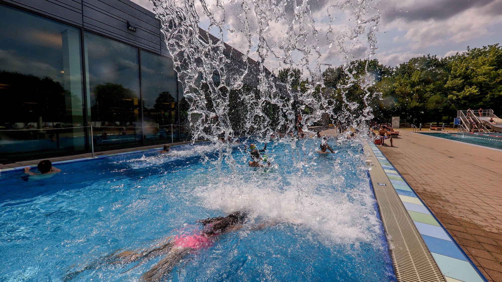 Im Schwimmbad taucht eine Besucherin unter einem Wasserfall hindurch.