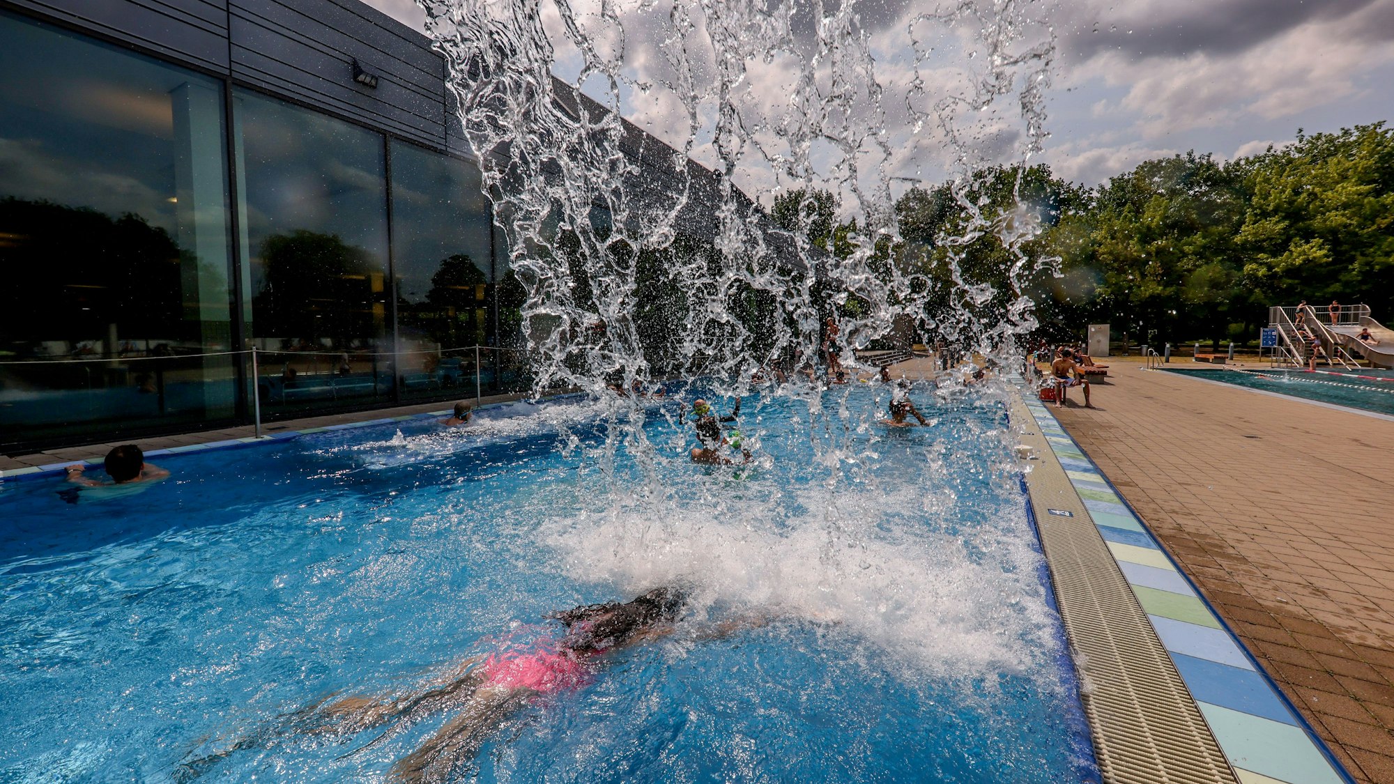 Im Schwimmbad taucht eine Besucherin unter einem Wasserfall hindurch.