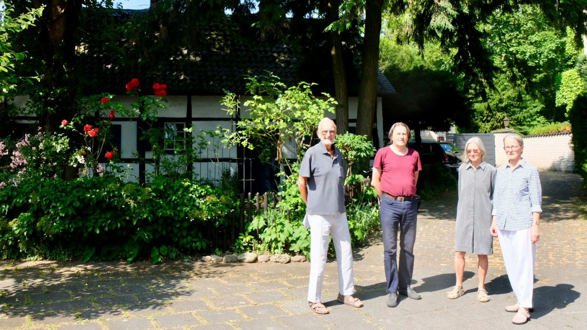 Zwei Männer und zwei Frauen stehen vor einem Fachwerkhaus im Grünen.