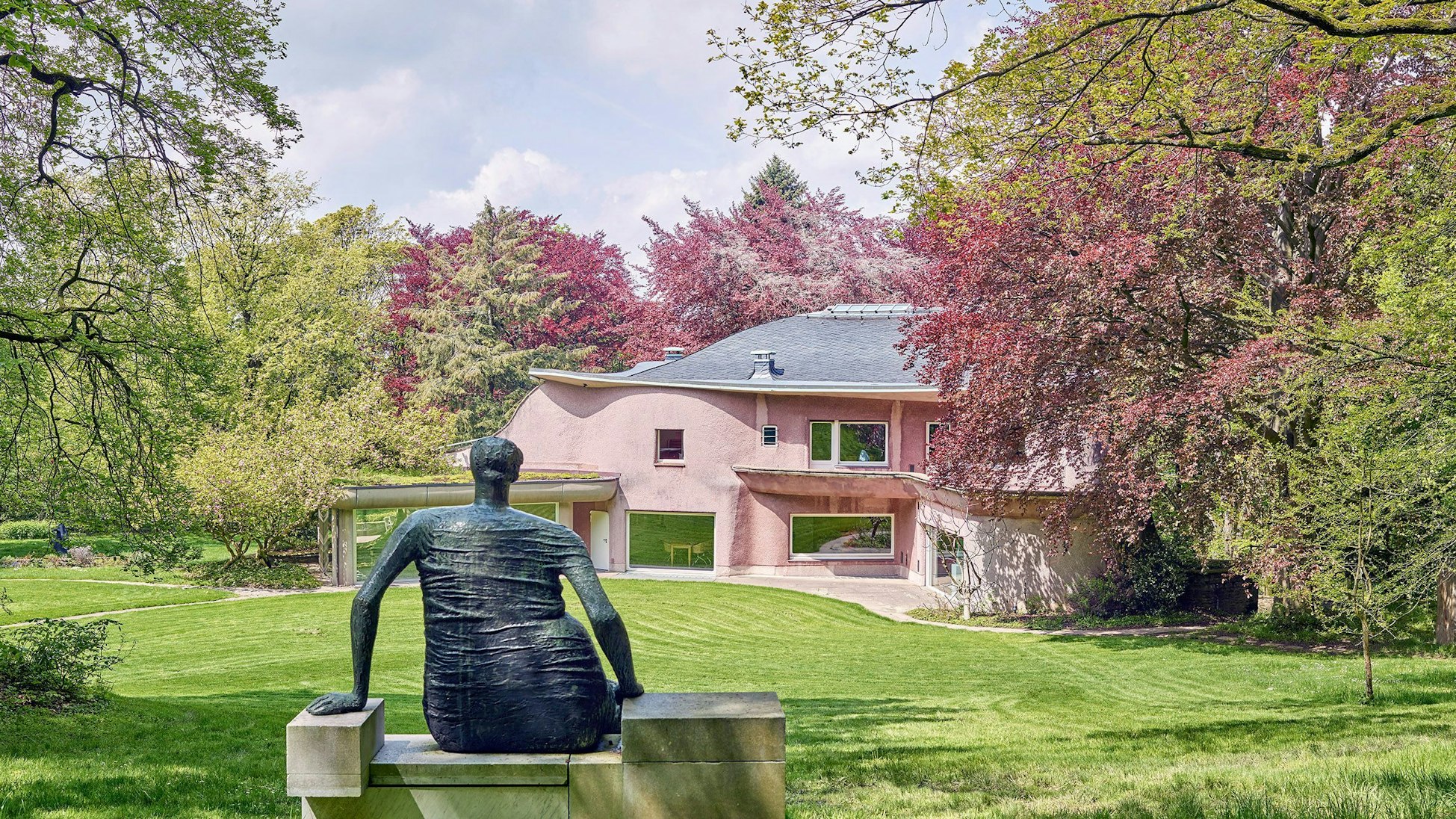 Eine Skulptur steht vor einer alten Villa und blühenden Bäumen.