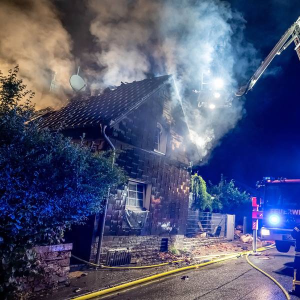 Ein Feuerwehrauto steht mit ausgefahrener Drehleiter an einem Haus, aus dem Rauch aufsteigt.