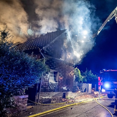 Ein Feuerwehrauto steht mit ausgefahrener Drehleiter an einem Haus, aus dem Rauch aufsteigt.