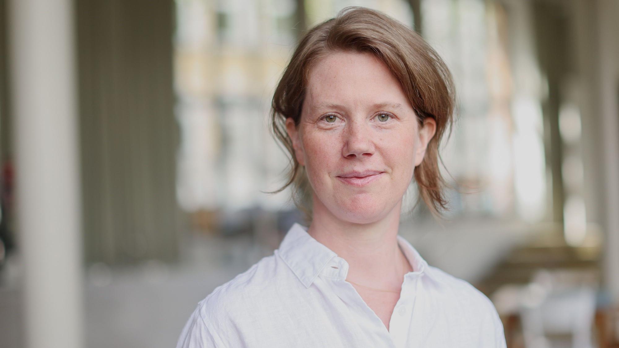 Vera Schöpfer hat die Haare hinten zusammengebunden. Sie steht im Foyer des Filmhauses und trägt ein weißes Hemd.