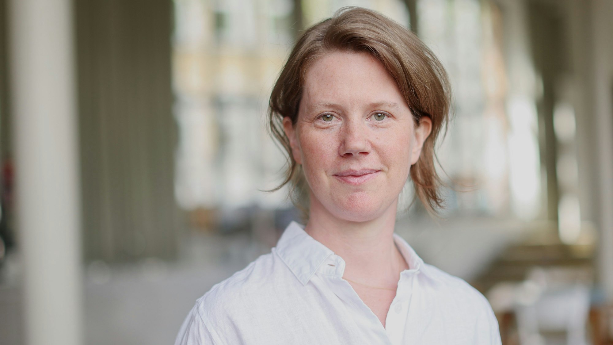 Vera Schöpfer hat die Haare hinten zusammengebunden. Sie steht im Foyer des Filmhauses und trägt ein weißes Hemd.