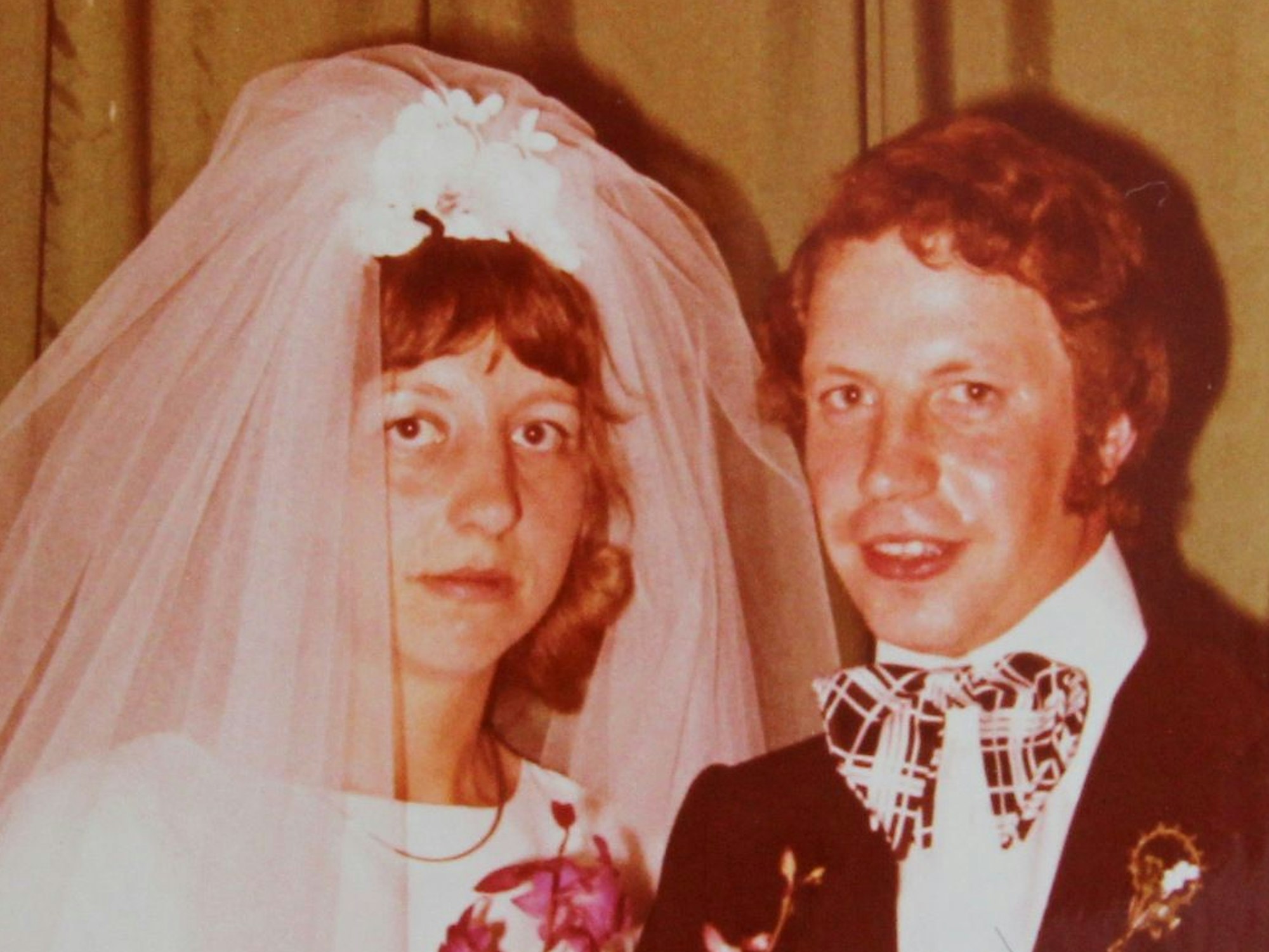 Das Foto zeigt das Ehepaar nach der kirchlichen Trauung. Die Braut trägt ein weißes Kleid und einen Schleier.