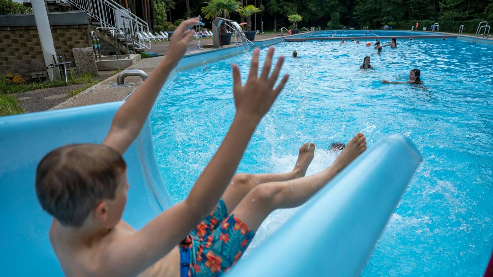 Eine Junge rutscht von einer Wasserrutsche ins Schwimmbecken.