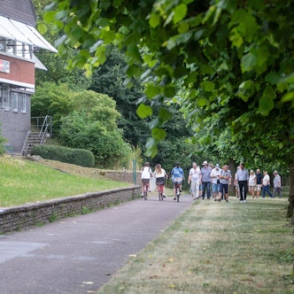 Radfahrer und Fußgänger sind auf einem Weg neben einer Grünfläche unterwegs.