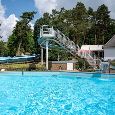 Ein Schwimmbecken und eine Rutsche umgeben von Bäumen.