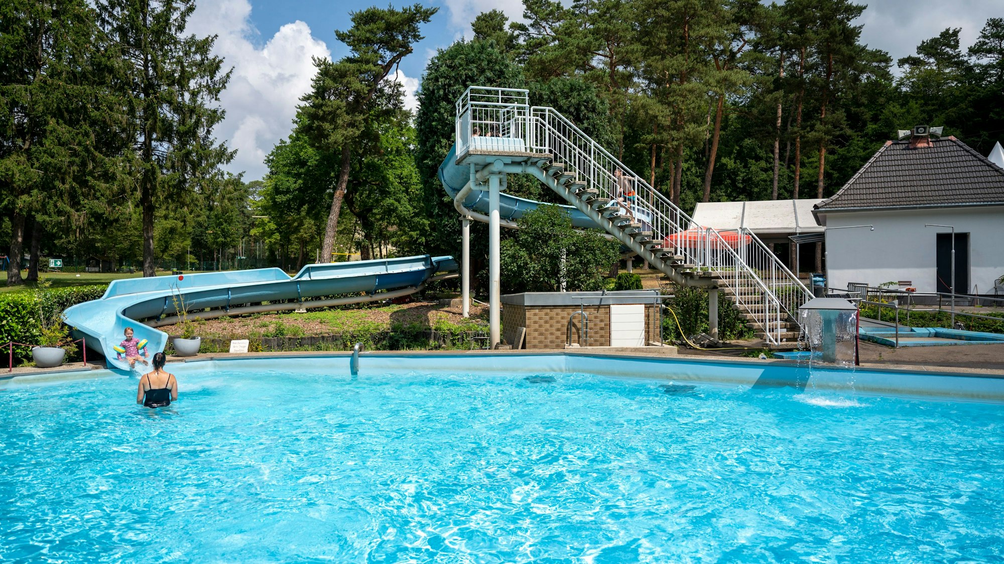 Ein Schwimmbecken und eine Rutsche umgeben von Bäumen.
