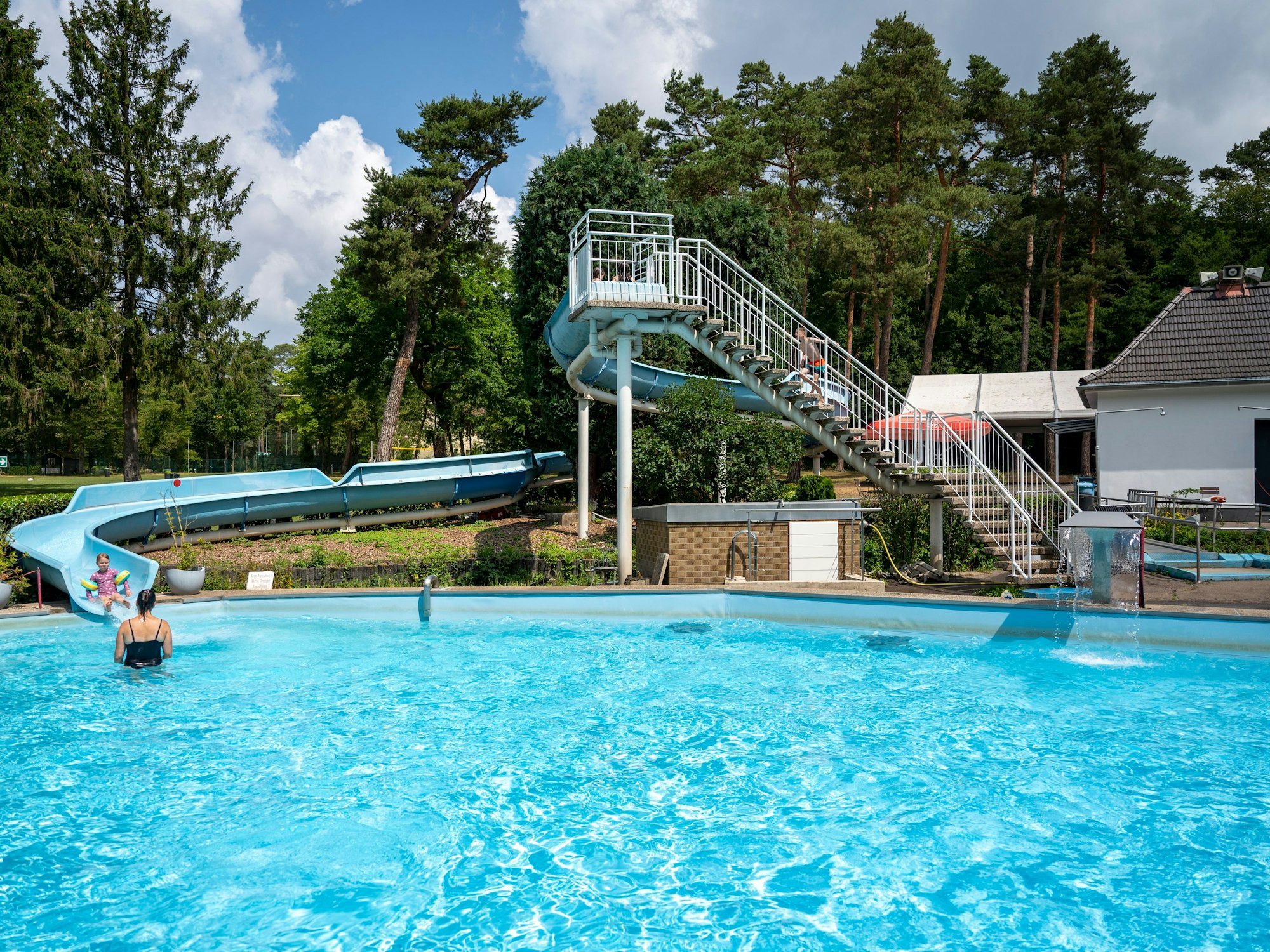 Das Waldbad Dünnwald: Ein Schwimmbecken mit einer Rutsche, im Hintergrund sind Bäume zu sehen.