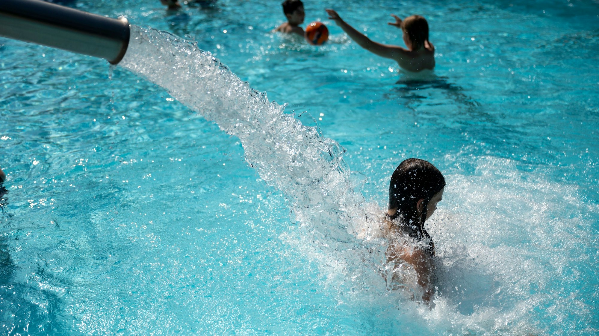 Ein Wasserstrahl schießt aus einem silbernen Rohr auf den Rücken einer jungen Frau.
