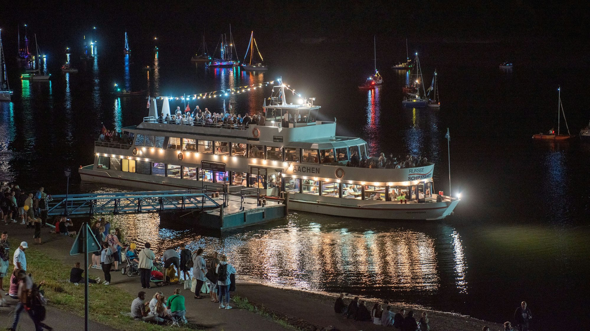 Ein beleuchtetes Schiff liegt bei Nacht am Ufer des Rursees.