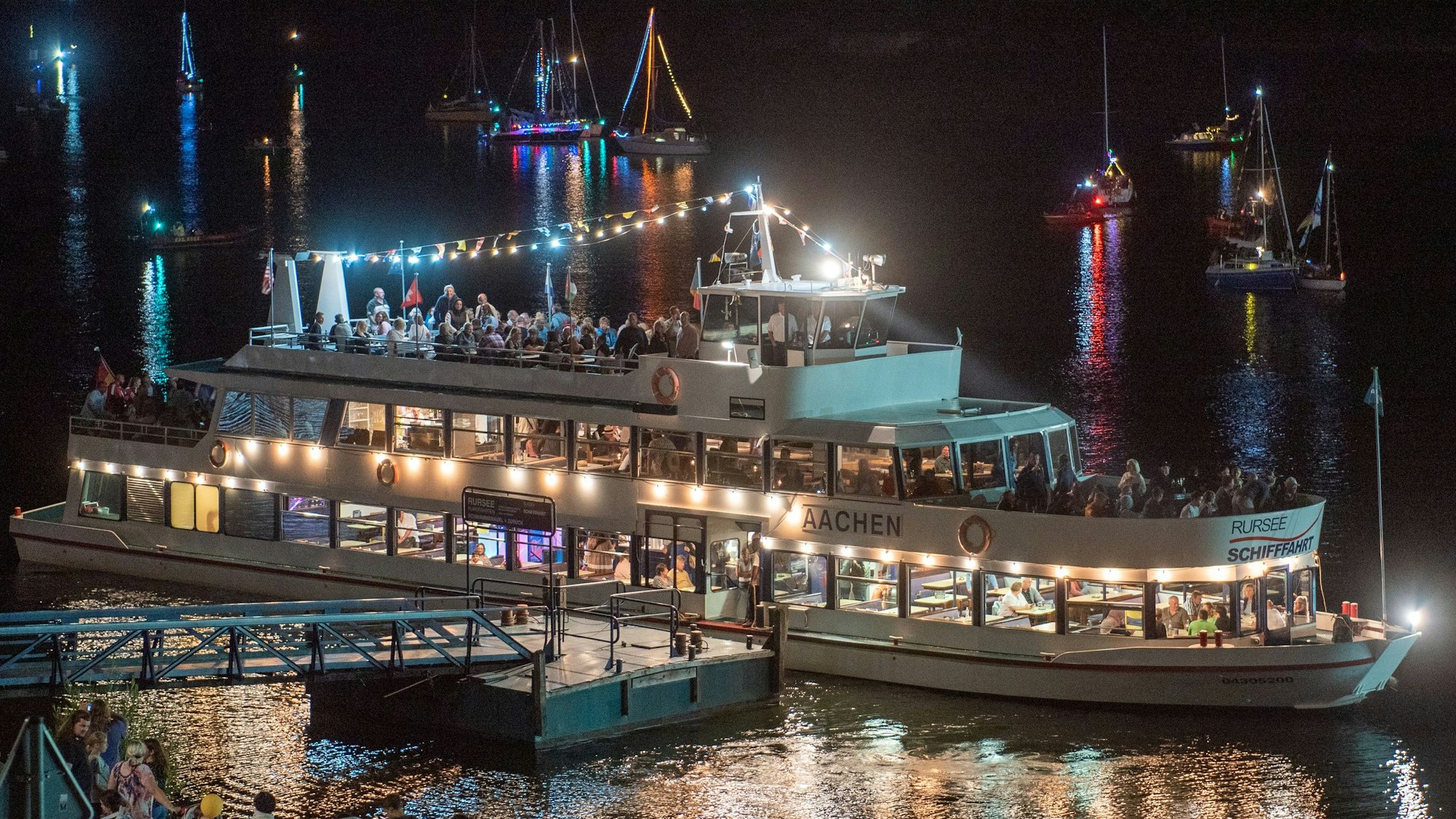 Es ist Nacht am Ufer des Rursees. Das Touristen-Schiff Stella Maris leuchtet hell auf dem Wasser.