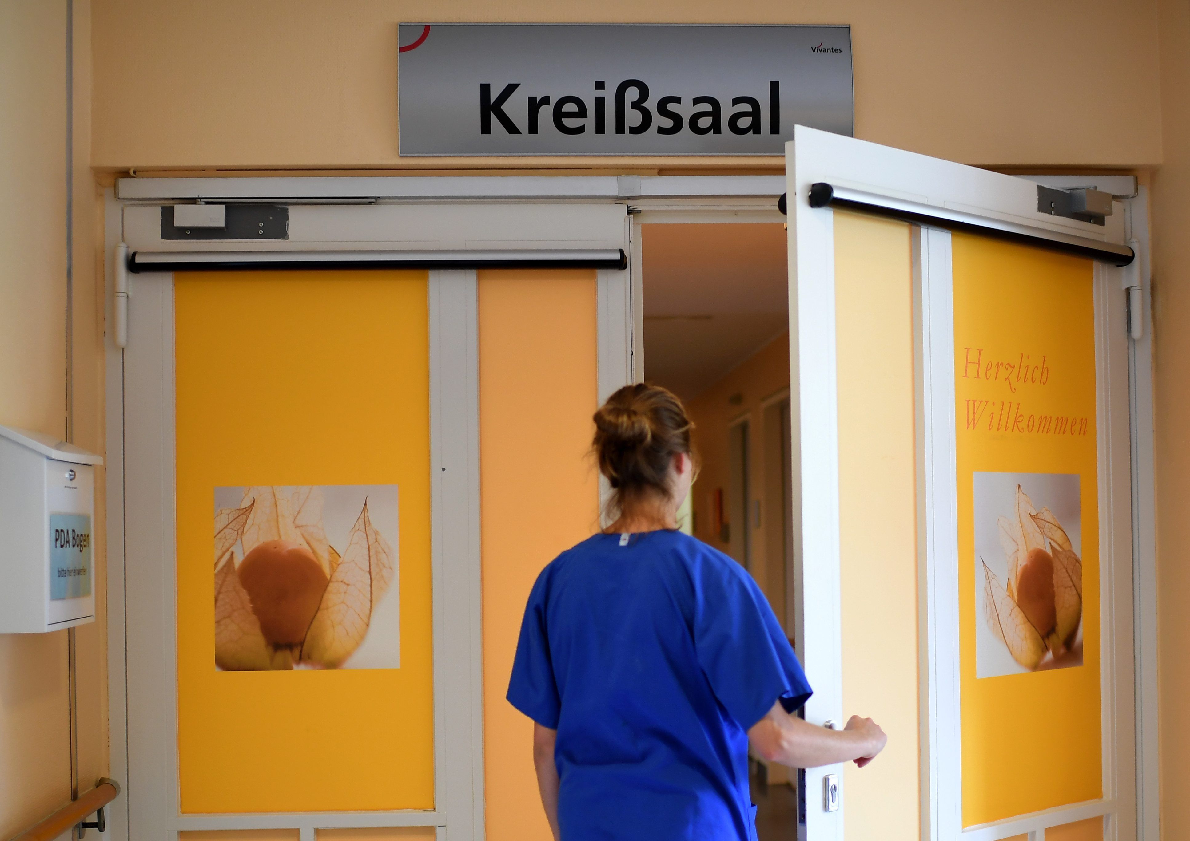Eine Mitarbeiterin steht vor einem Kreißsaal in einem Krankenhaus