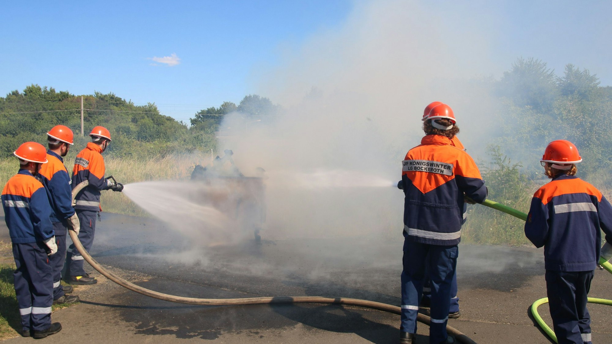 Mehrere Feuerwehrleute hantieren mit Schläuchen und löschen einen Schaubrand.
