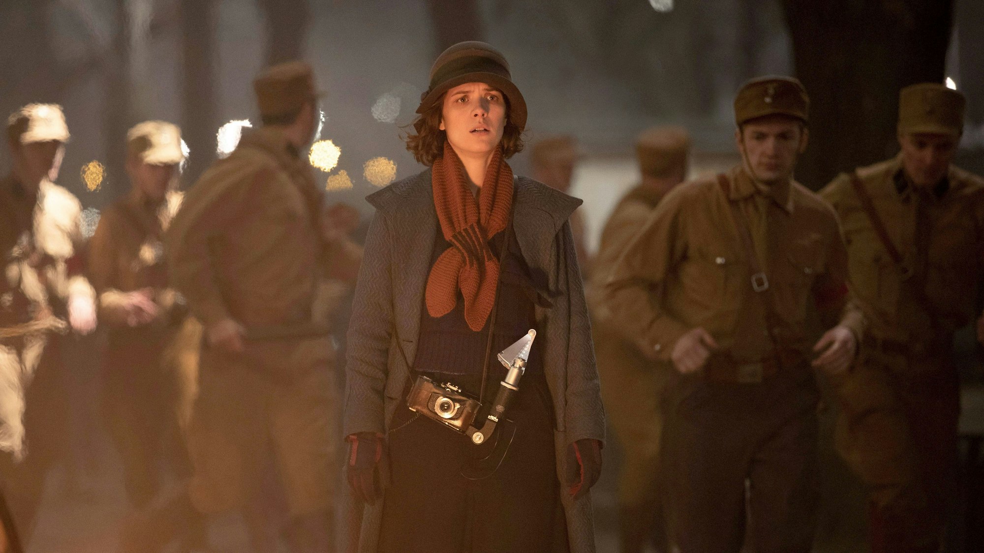 Zu sehen ist die Schauspielerin Liv Lisa Fries in ihrer Rolle als Charlotte Ritter. Im Hintergrund laufen einige Soldaten. Alle tragen Kleidung der späten 20er.
