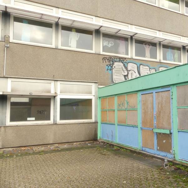 Ein schmuckloses Schulgebäude mit einem grün-blauen Anbau ist zu sehen.