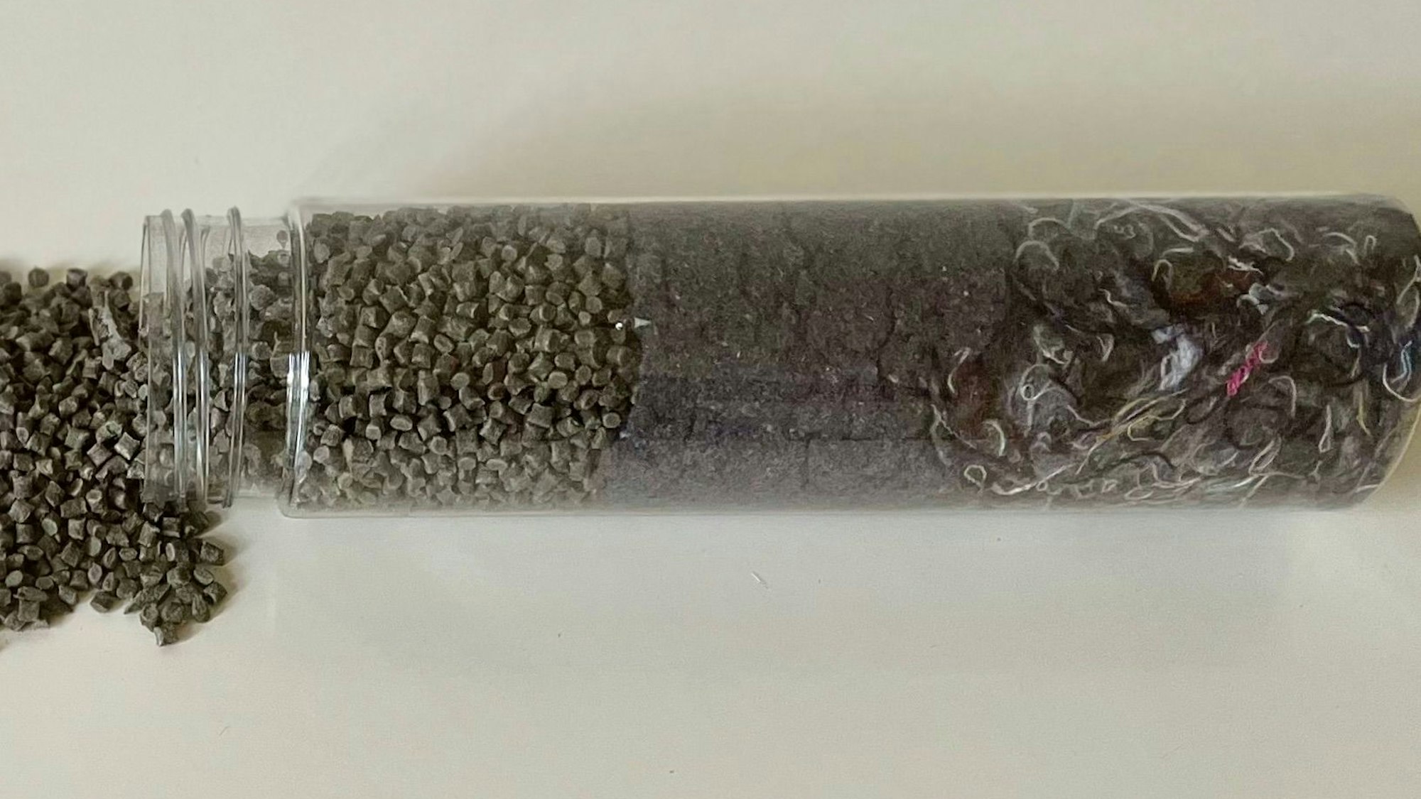 Rechts in der Flasche sind die Stoff-Fasern, in der Mitte die gemahlenen Fasern und links das Endprodukt, das Granulat, zu sehen.