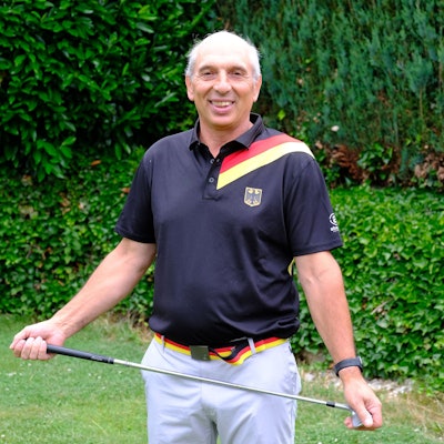 Der Golfspieler trägt ein Poloshirt mit Bundesadler und den deutschen Farben und hält einen Golfschläger in den Händen.