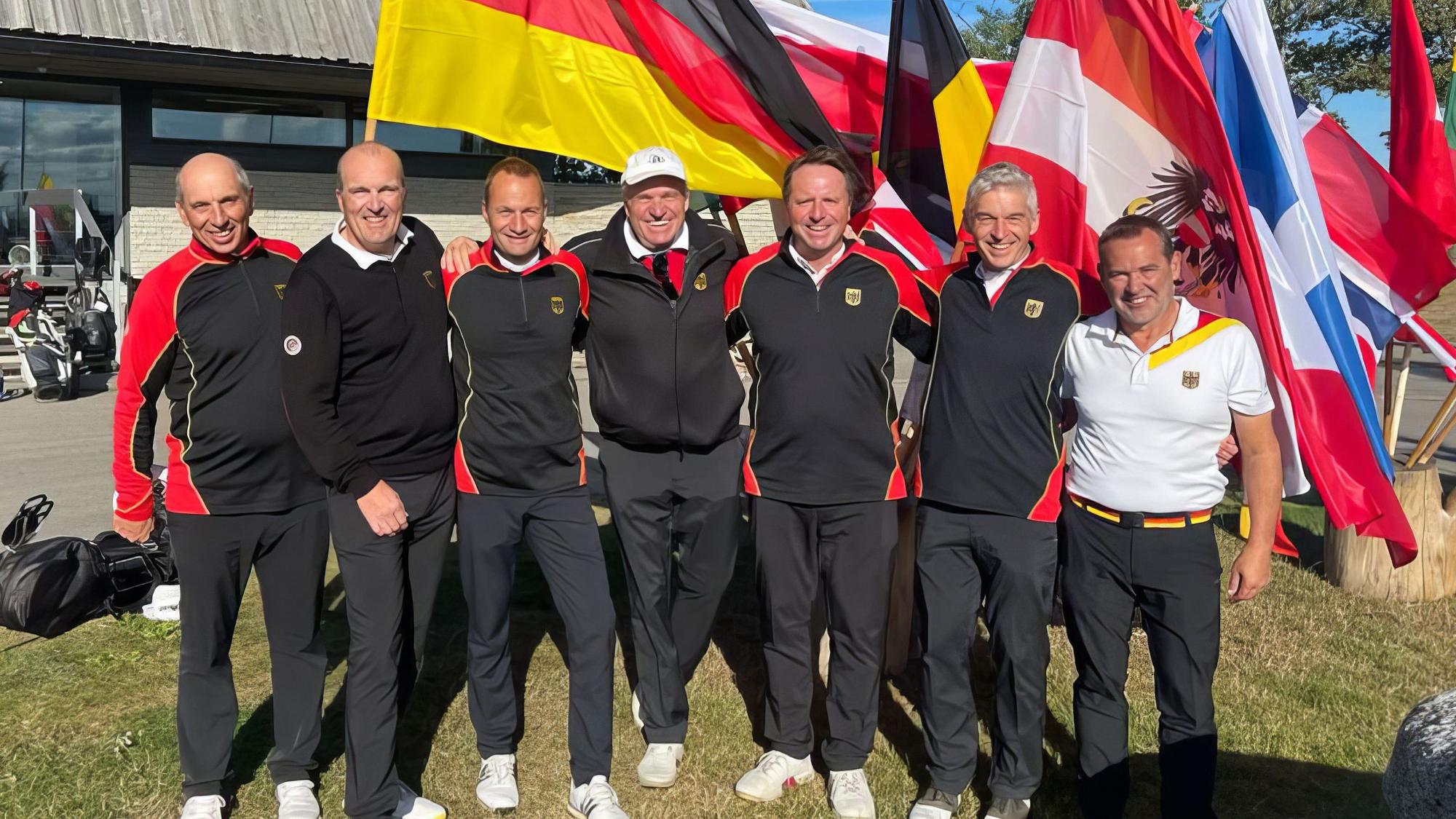 Das Nationalteam in Trainingsanzügen vor der deutschen Flagge.