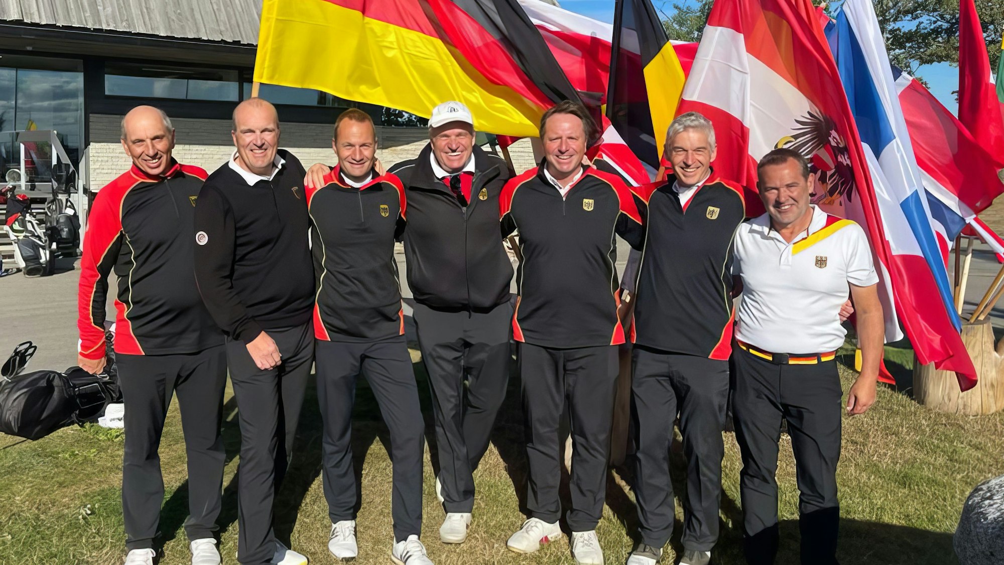Das Nationalteam in Trainingsanzügen vor der deutschen Flagge.