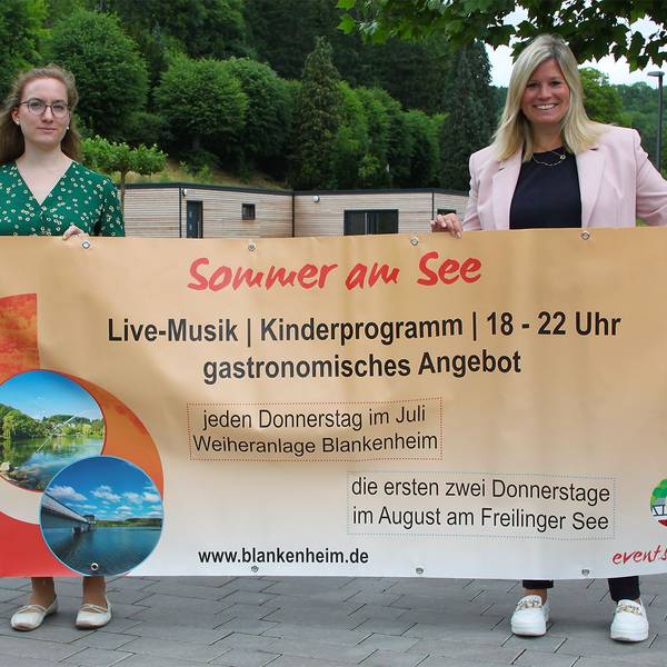 Zwei Frauen halten ein großes Veranstaltungs-Transparent in die Höhe.