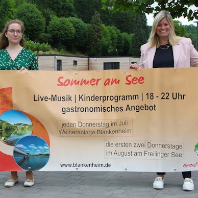 Zwei Frauen halten ein großes Veranstaltungs-Transparent in die Höhe.