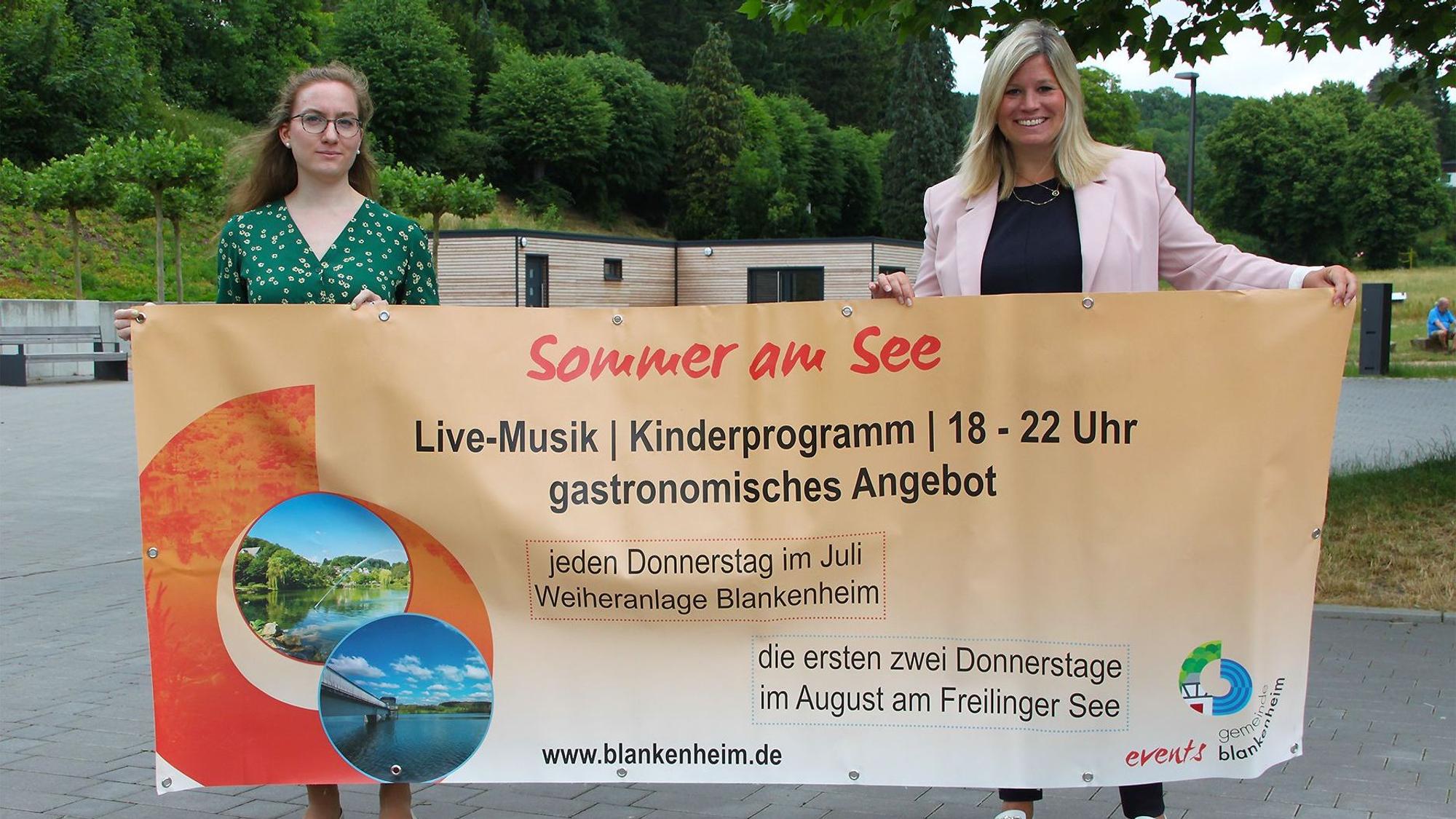 Zwei Frauen halten ein großes Veranstaltungs-Transparent in die Höhe.