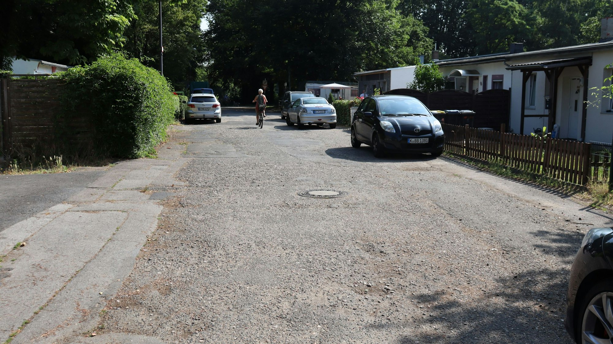 Eine Straße mit unebener Asphaltdecke mit am Straßenrand parkenden Autos ist zu sehen.