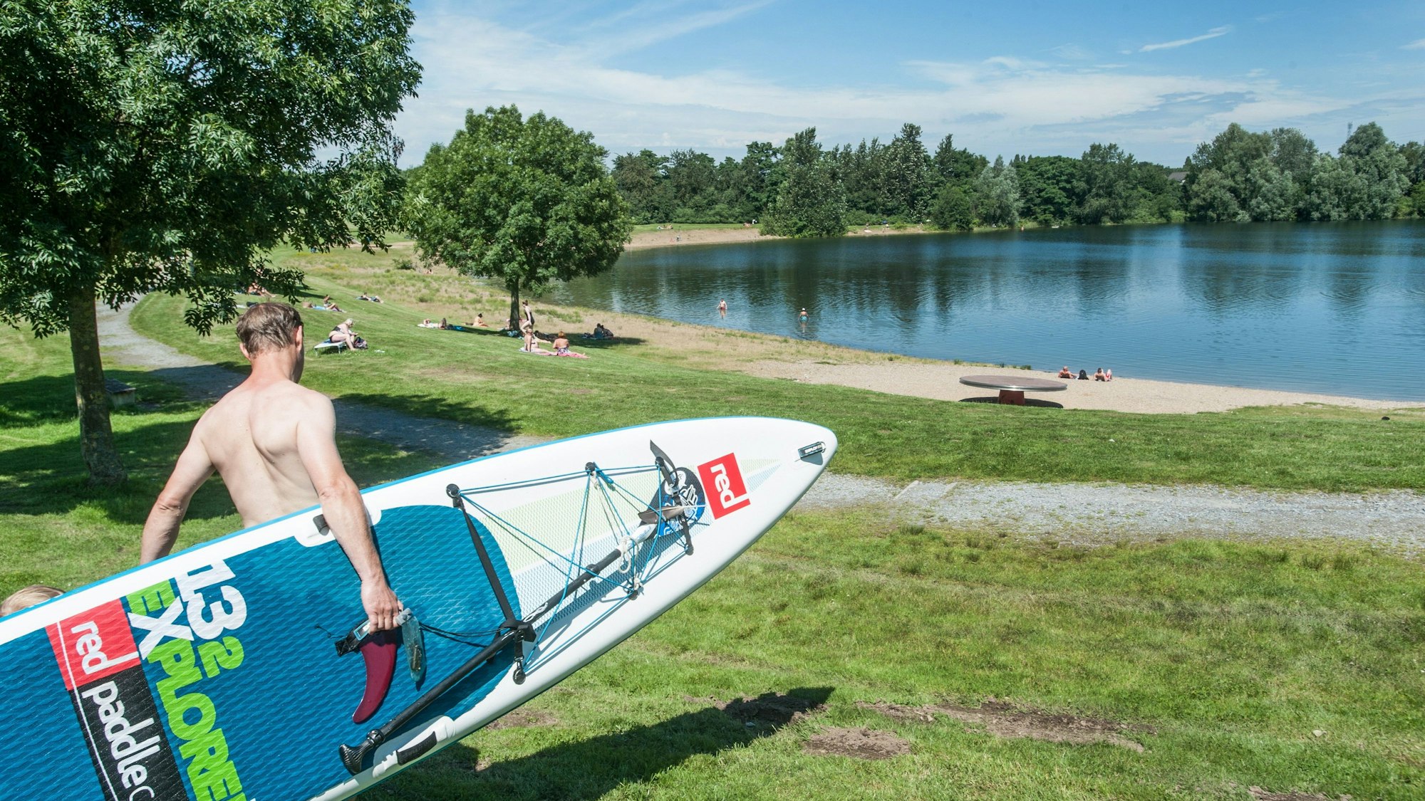 Ein Stand-Up-Paddler trägt sein Board zum Ufer des Hitdorfer Sees in Leverkusen.