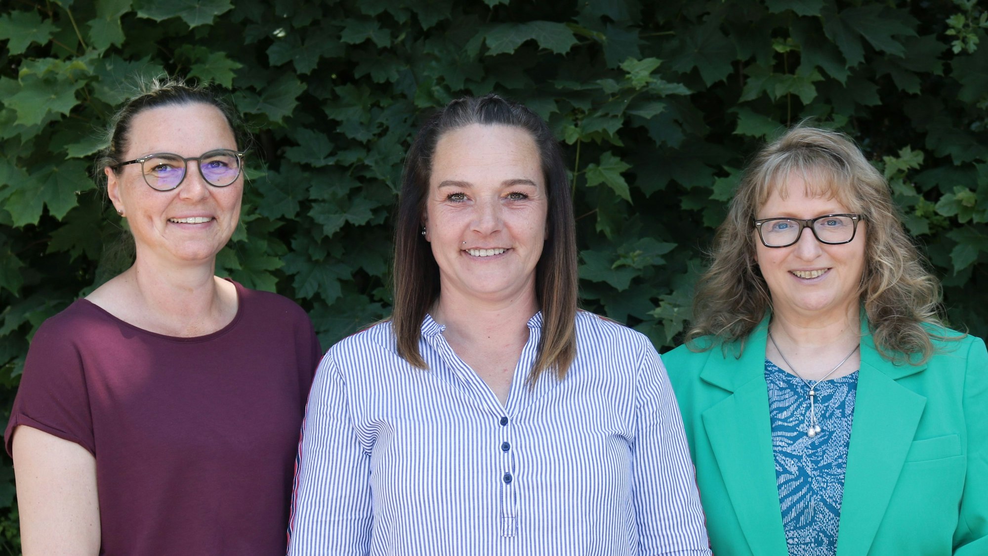 Drei Frauen vor einer Blätterwand.