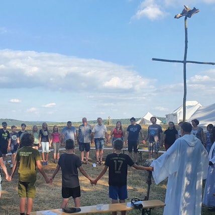 Kinder und Jugendliche halten sich bei einem Gottesdienst unter freiem Himmel an den Händen.