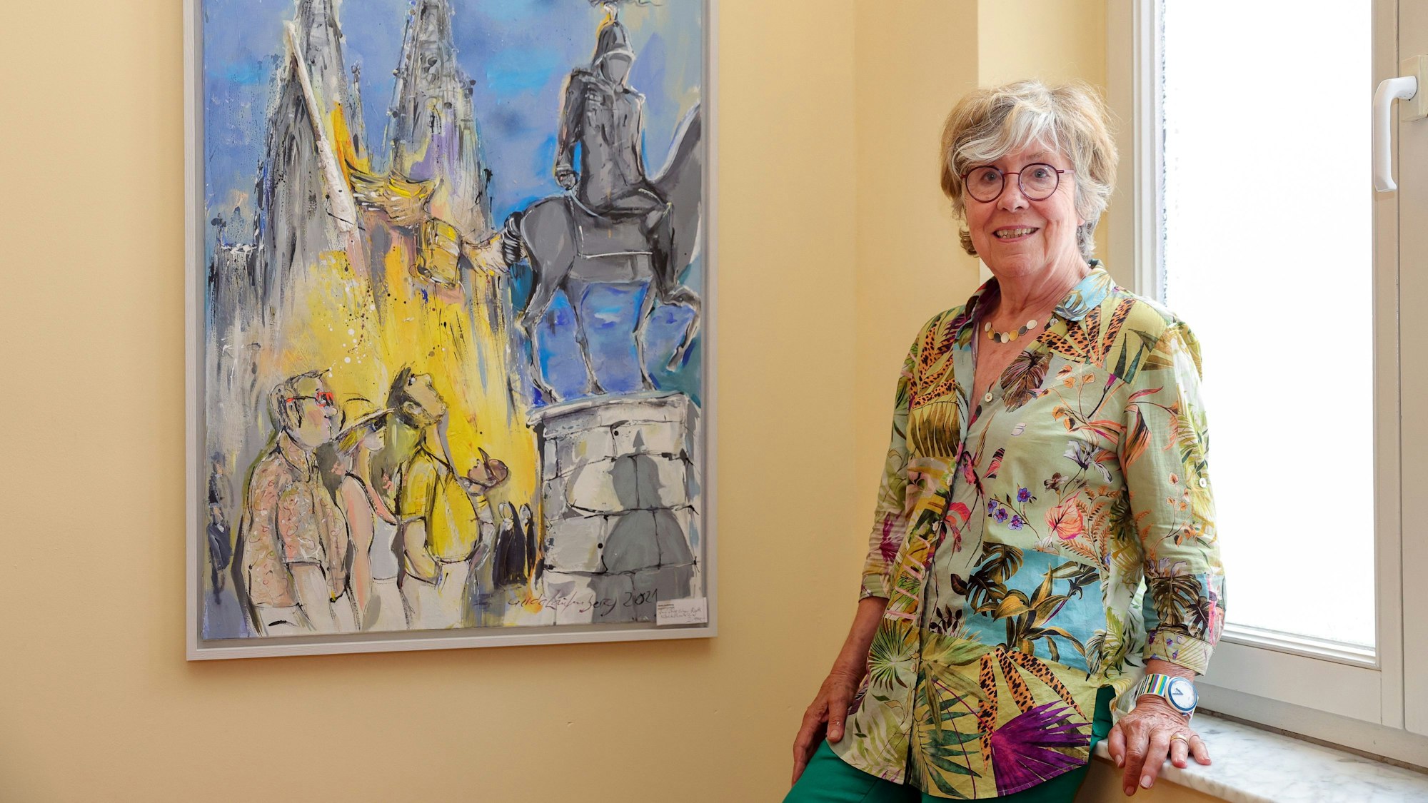 Gerda Laufenberg lehnt neben einem Kölnbild an einer Fensterbank.