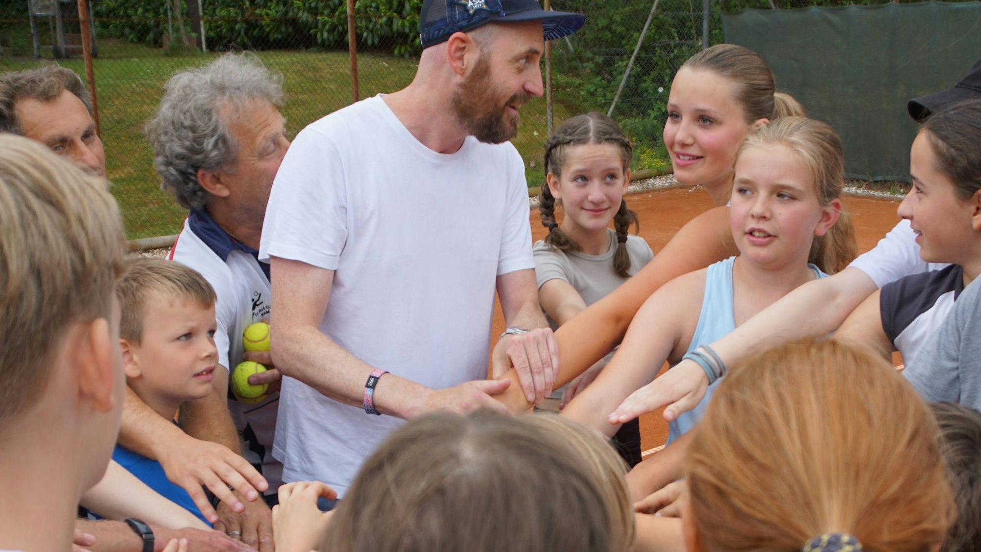 Die Kinder des TC Rot-Gold stehen auf dem Tennisplatz im Kreis. Sie stehen eng aneinander und halten ihre ausgestreckten Arme in die Mitte.