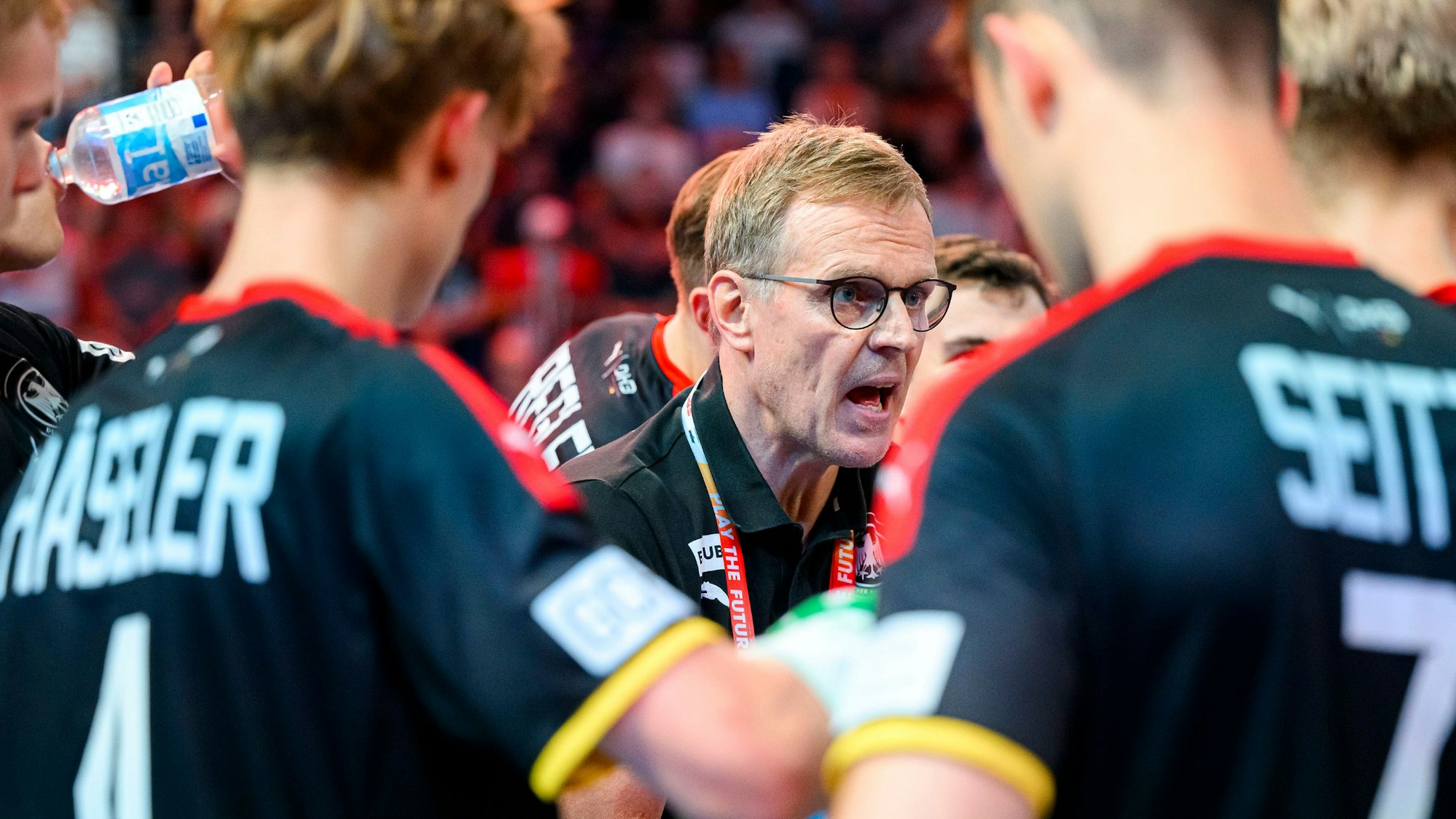 Bild einer Handball-Mannschaft, die sich mit dem Trainer in der Mitte bespricht.