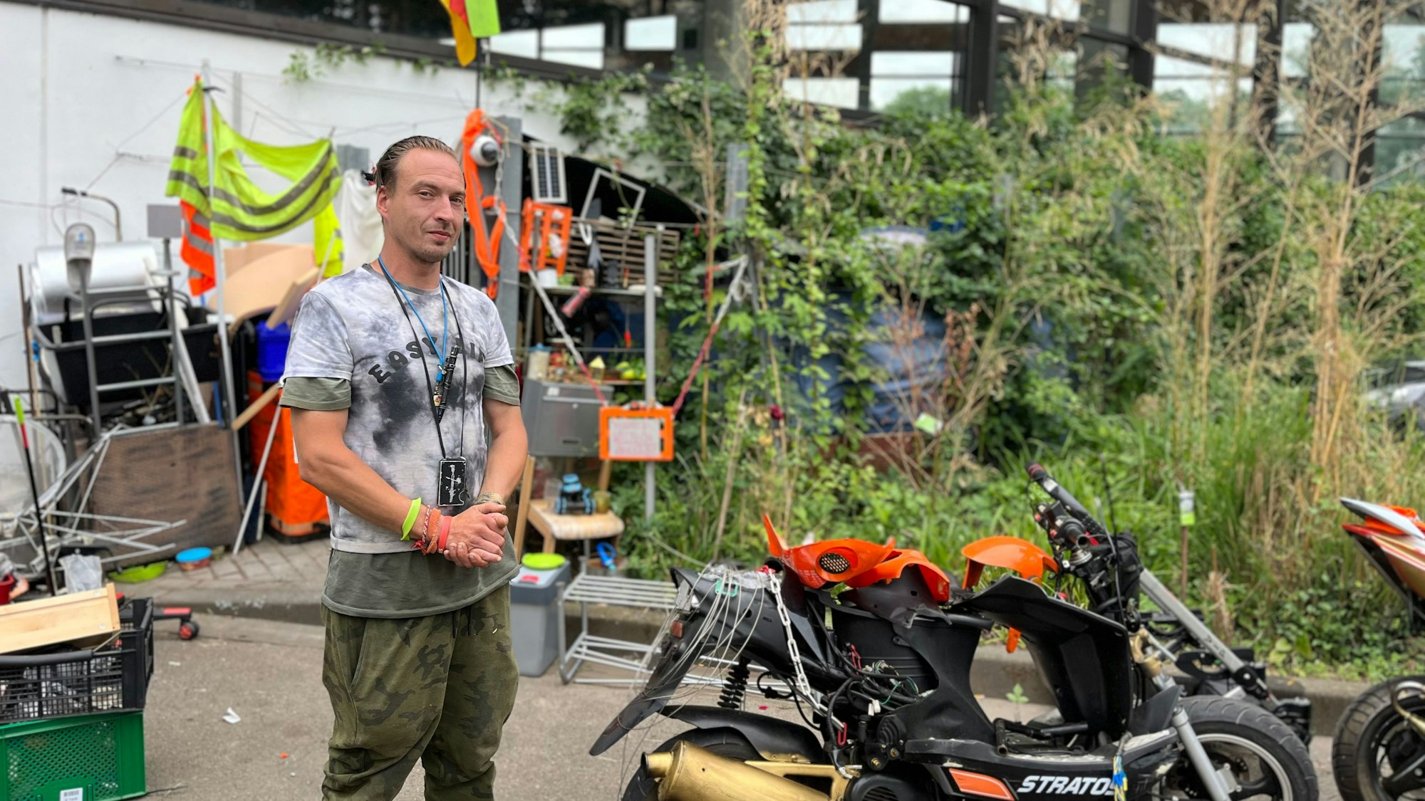 Der Obdachlose Marcel K. steht vor seiner Hütte am Höhenbergbad. Neben ihm ein Motorroller.