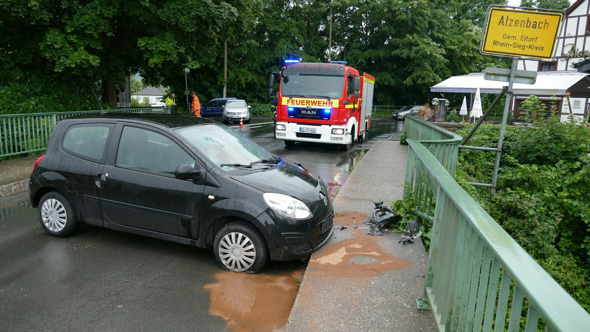 Ein Renault Twingo steht quer auf einer Brücke, vor dem Fahrzeug liegen Autoteile. Die Feuerwehr steht im HIntergrund.