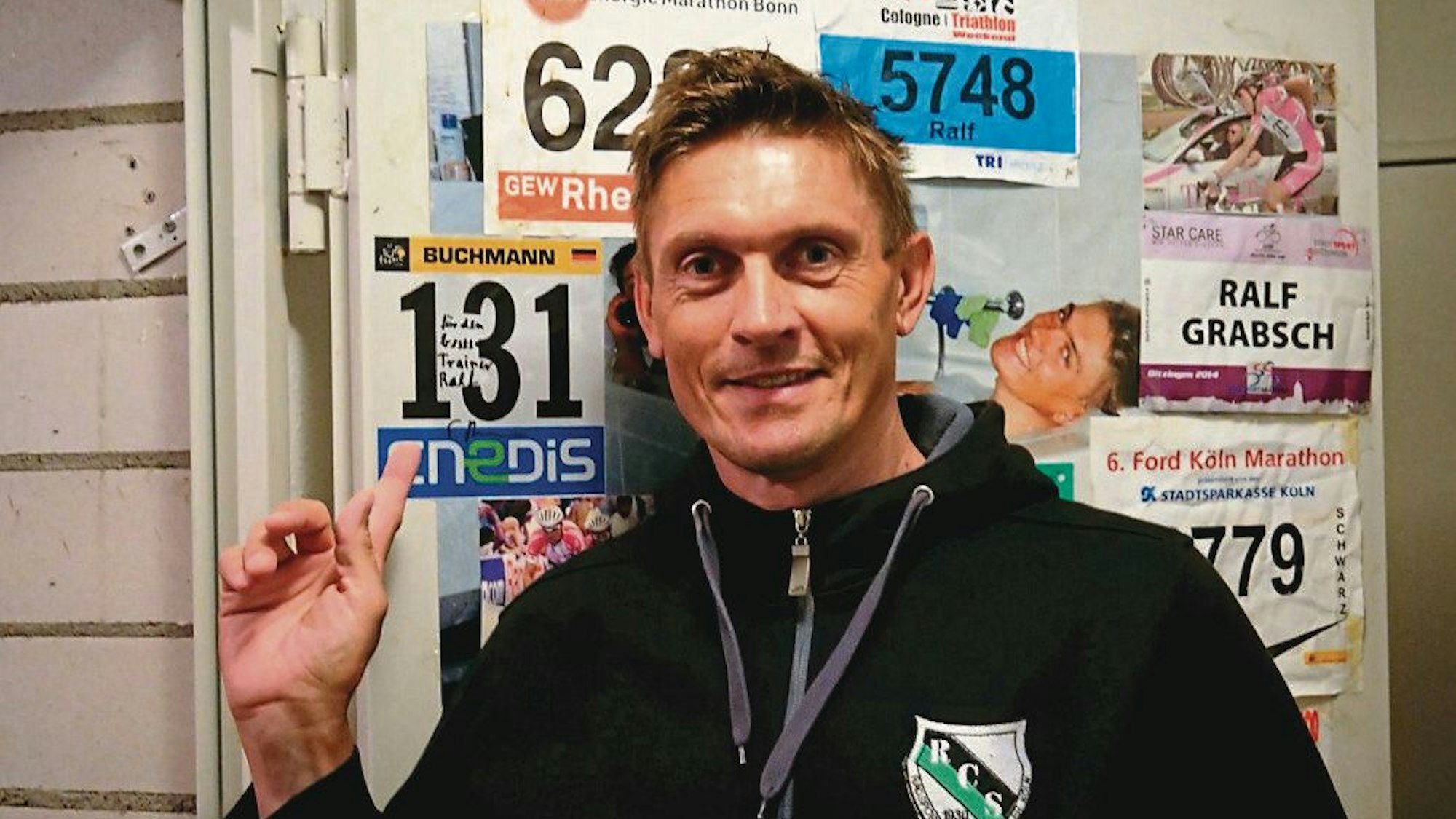 Ein Mann in Trainingsjacke vor einer Wand mit Startnummern.