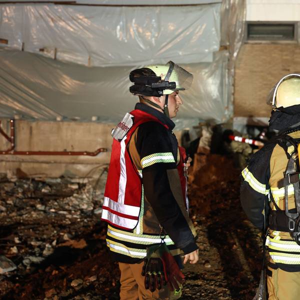 Drei Feuerwehrleute vor dem Eingang zur Turnhalle, vor dem ein Lüfter in Stellung gebracht wurde.