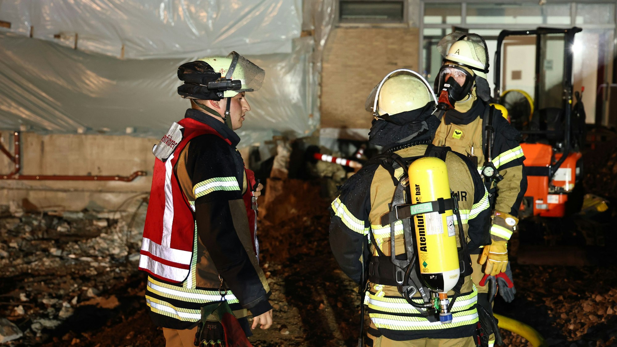 Drei Feuerwehrleute vor dem Eingang zur Turnhalle, vor dem ein Lüfter in Stellung gebracht wurde.