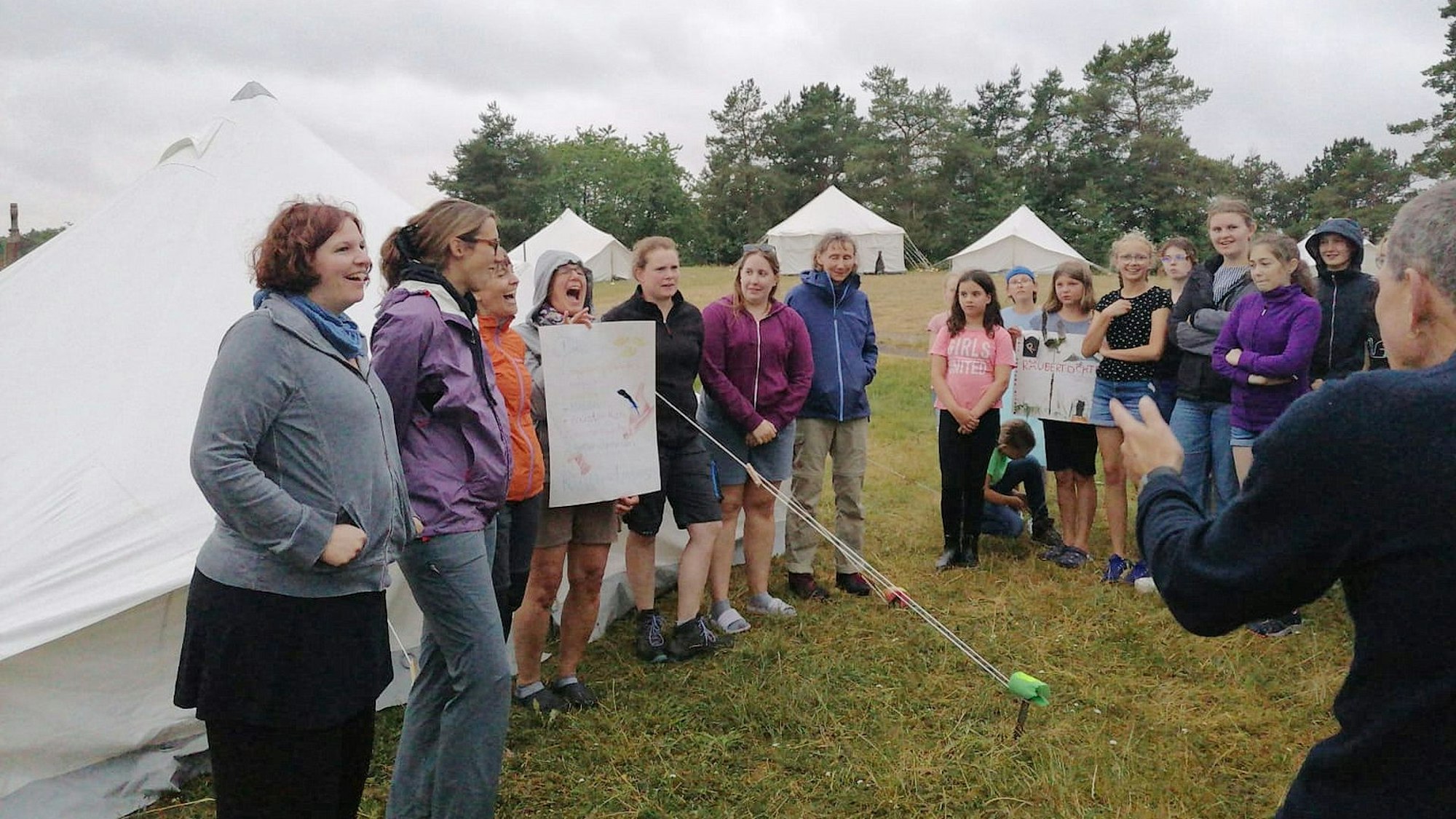 Teilnehmer eines Jugendzeltlagers stehen auf einer Wiese mit weißen Zelten.
