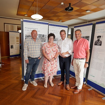 Drei Männer und eine Frau stehen vor den Stellwänden einer Ausstellung.